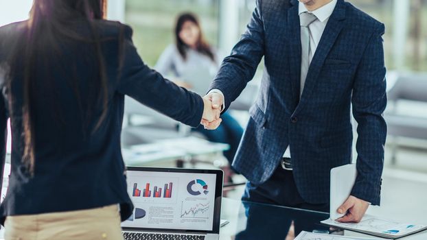 in the foreground is shaking hands with financial partners near the workplace in the modern office