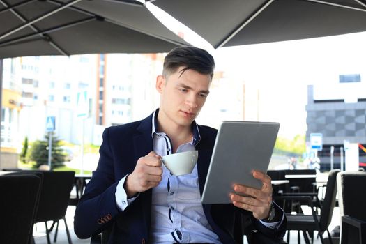 Businessman drinking coffee and reading news in cafe.