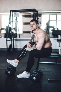 brooding male bodybuilder sitting on a bench after a workout in the fitness centre