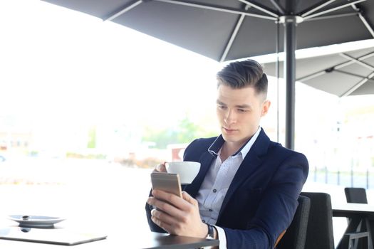 business man drinking a cup of coffee while sitting with his phone in cafe.