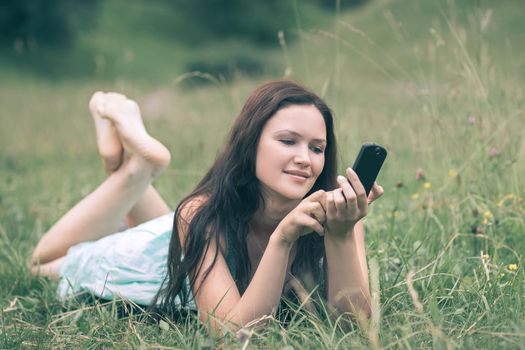 attractive young woman using her smartphone while lying in a clearing . people and technology