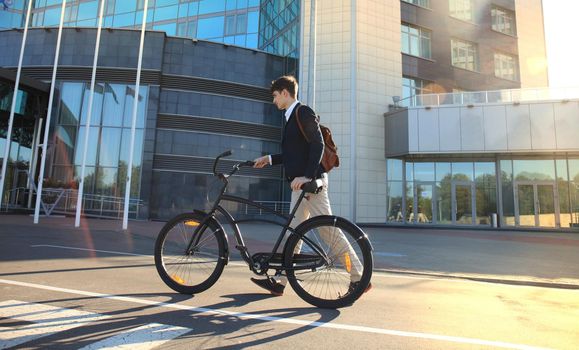 Confident young businessman walking with bicycle on the street in town.