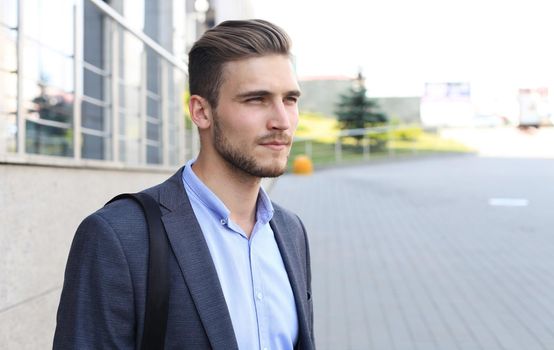Portrait of a handsome businessman in a suit standing outside a city building.