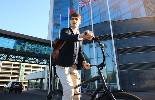 Confident young businessman walking with bicycle on the street in town.