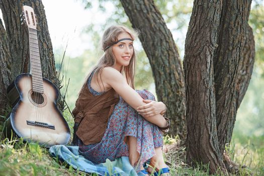 attractive young hippie woman sitting near a tree in the forest