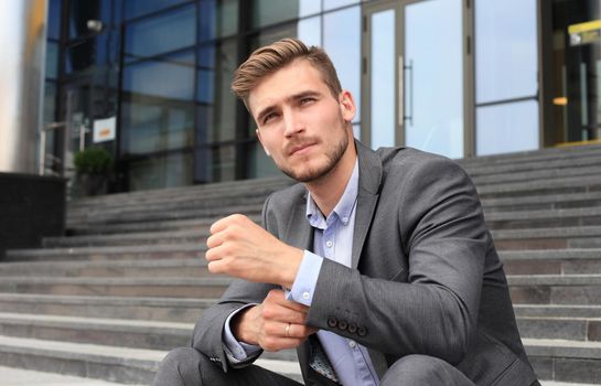 Handsome male business executive sitting on stairs outside a building.