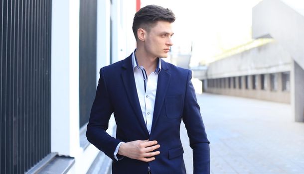 Portrait of a handsome businessman in a suit standing outside a city building