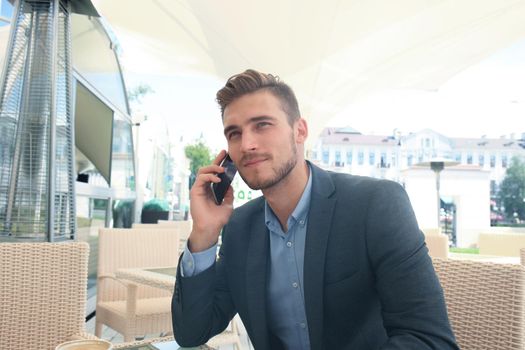 business man drinking a cup of coffee while sitting with his phone in cafe.