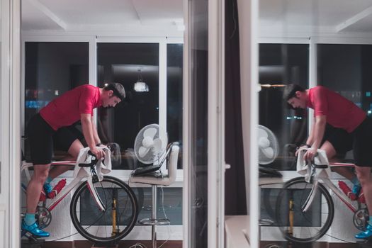 Man cycling on the machine trainer he is exercising in the home at night. Playing online bike racing game during coronavirus covid19 lockdown. New normal concept.