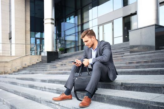 Handsome male business executive sitting on stairs outside a building.