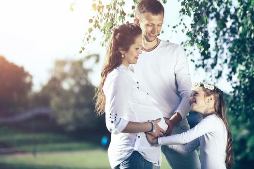 happy family pregnant mom,dad and little daughter on a walk in the Park on a Sunny day