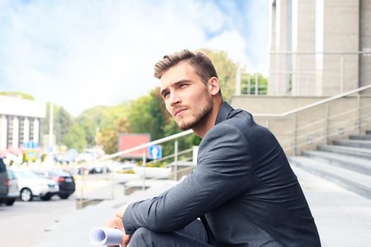 Handsome male business executive sitting on stairs outside a building.