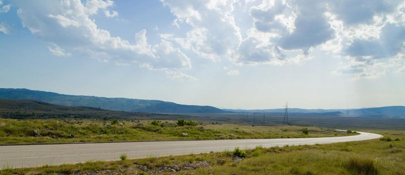 Evening summer landscape with green grass, road and clouds