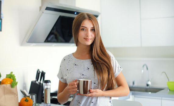 Young woman holding grocery shopping bag with vegetables standing in the kitchen