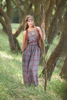 young hippie woman with a long stick walking through the forest . the concept of unity with nature