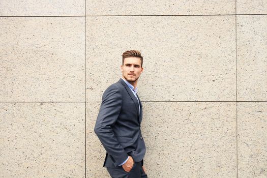 Portrait of a handsome businessman in a suit standing outside a city building.