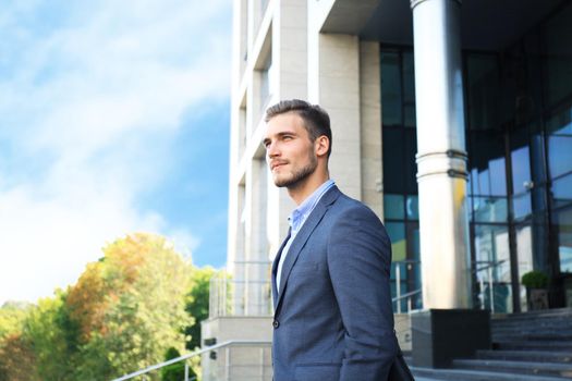 Portrait of a handsome businessman in a suit standing outside a city building.