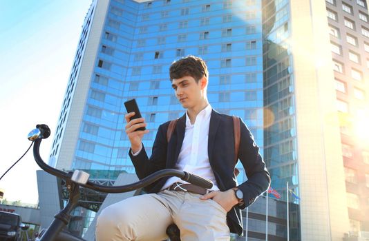 Young businessman with bicycle and smartphone on city street.