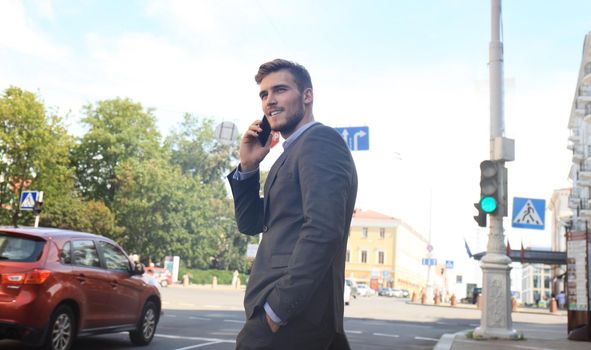 Young handsome businessman crossing the street using mobile phone.