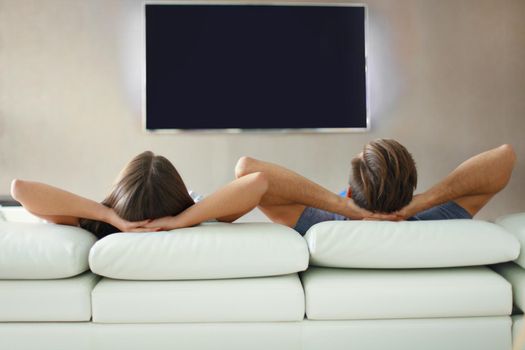 Rear view of a couple relaxing on a sofa and watching TV at home