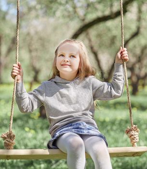 smiling little girl sitting on a swing in the garden. the concept of children's happiness