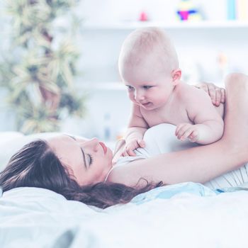 happy mother and year-old baby playing on bed in bedroom