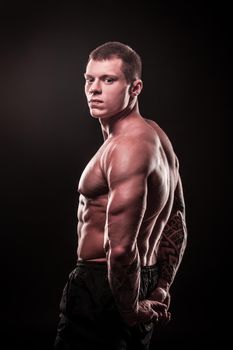 side view. male bodybuilder holding his hands behind his back .isolated on black background