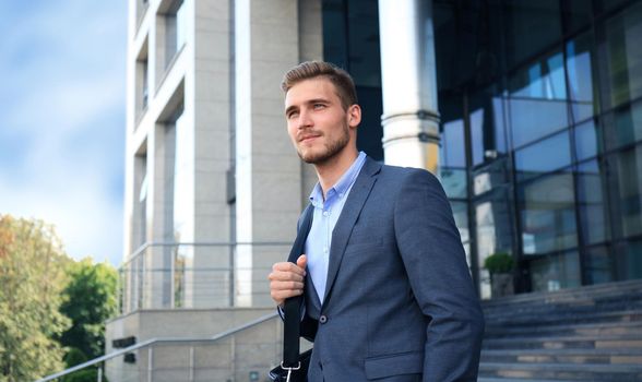 Portrait of a handsome businessman in a suit standing outside a city building.