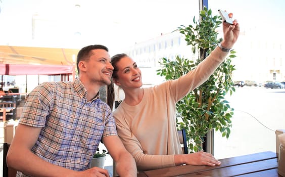 Beautiful young couple is making selfie using a smartphone and smiling while sitting in the cafe.