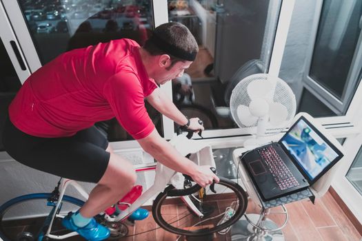 Man cycling on the machine trainer he is exercising in the home at night. Playing online bike racing game during coronavirus covid19 lockdown. New normal concept.