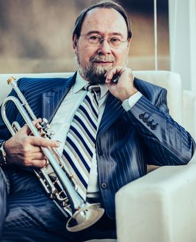 professional musician with a trumpet sitting in a chair, on the background of the concert hall