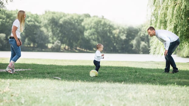 mother, father and their little son are playing with the ball on the lawn. the concept of active recreation