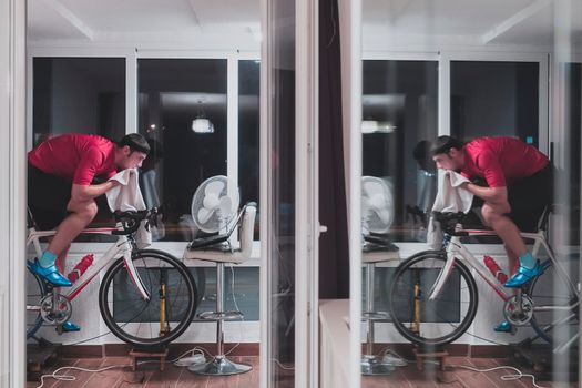 Man cycling on the machine trainer he is exercising in the home at night. Playing online bike racing game during coronavirus covid19 lockdown. New normal concept.