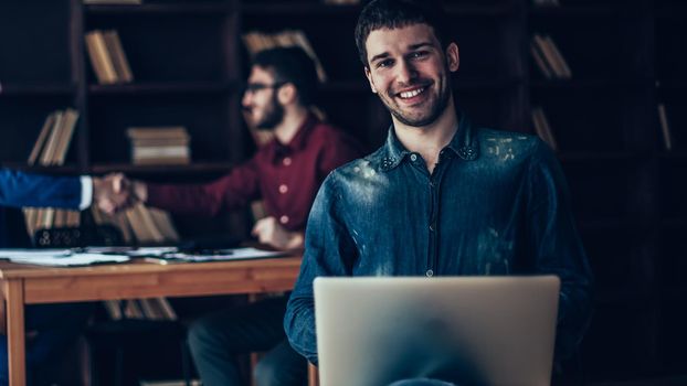 creative sales Manager with notebook on background of business partners handshaking in a modern office