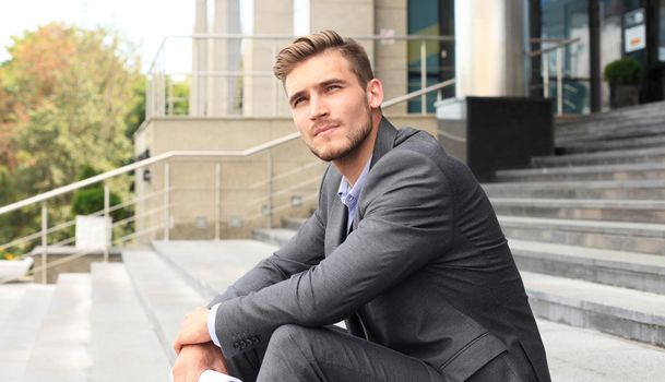 Handsome male business executive sitting on stairs outside a building.