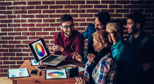 team of designers in the workplace in front of the open laptop is discussing a new color palette in a modern office