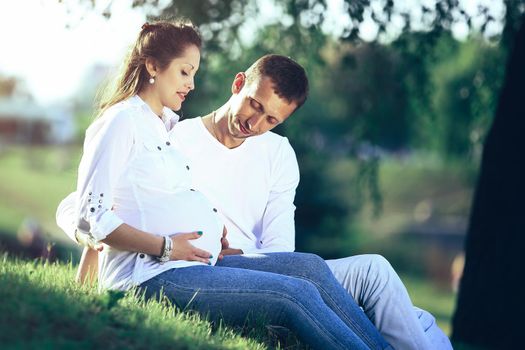 pregnant woman and happy future father sitting on the grass in the Park on a Sunny day