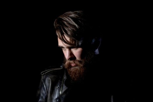 brooding bearded hipster in a leather jacket looking somewhere to the side. isolated on black background