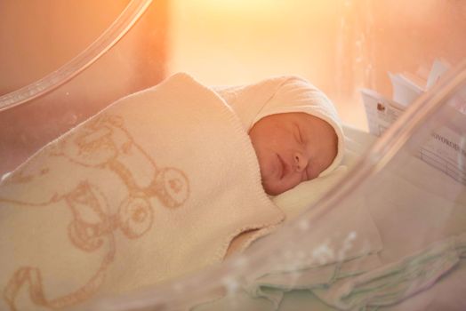 newborn baby child sleeping in plastic bed at hospital  wearing blanket coat