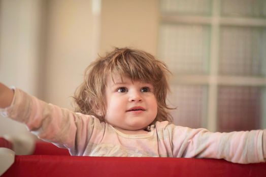 little baby girl with strange hairstyle and curlers in bed at home