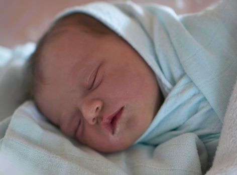 newborn baby child sleeping in plastic bed at hospital  wearing blanket coat
