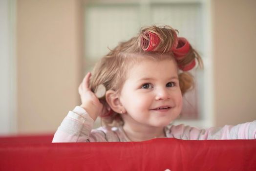 little baby girl with strange hairstyle and curlers in bed at home