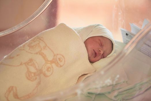 newborn baby child sleeping in plastic bed at hospital  wearing blanket coat