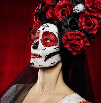 portrait of a beautiful woman with a sugar skull makeup with a wreath of flowers on her head, red background