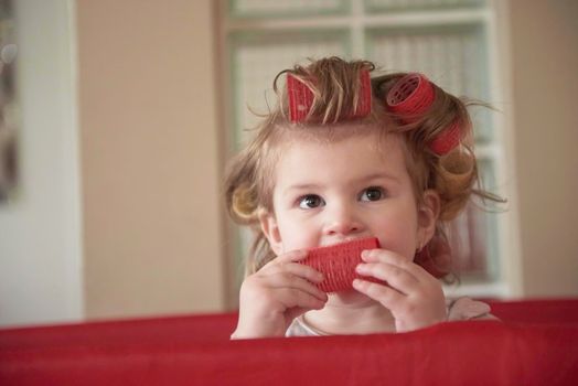 little baby girl with strange hairstyle and curlers in bed at home