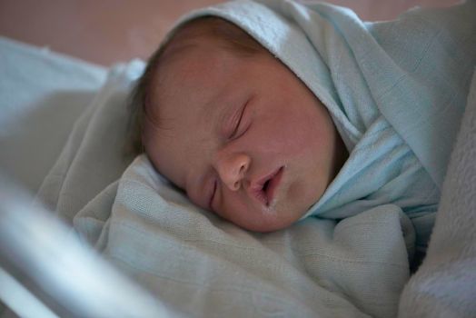 newborn baby child sleeping in plastic bed at hospital  wearing blanket coat