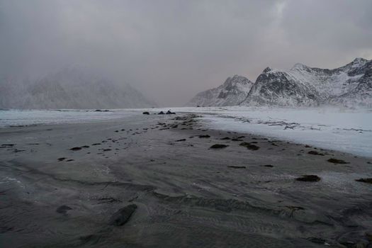 scandinavian coast at winter with mountains covered with snow in background and bad cloudy weather