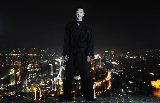 ninja assasin hold katana samurai old martial weapon swordat night with city lights in background