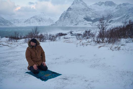 Muslim traveler praying in cold snowy winter day near the car in Scandinavia