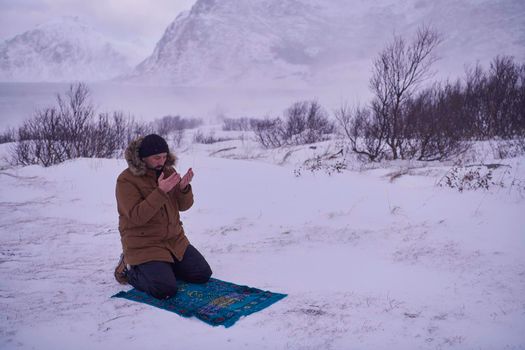 Muslim traveler praying in cold snowy winter day near the car in Scandinavia